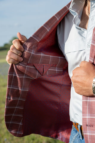 Cowboy wearing a red plaid shirt with a white shirt underneath, standing outdoors.