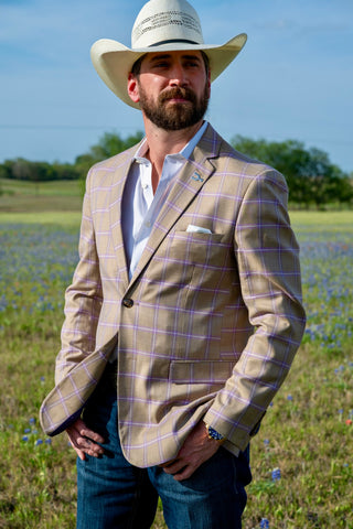 Man wearing a beige checkered blazer, white shirt, and cowboy hat standing in a field with bluebonnets.
