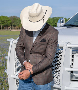 Person wearing a brown plaid blazer and white cowboy hat standing in front of a white truck.