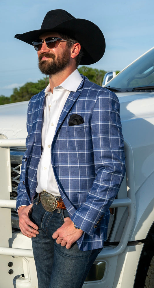 Man wearing a blue checkered blazer and black cowboy hat standing next to a white ford truck. This cowboy sport coat is a modern fit, styled with blue jeans and cowboy belt buckle. 