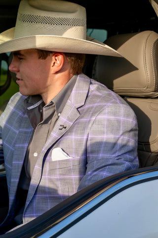 Man wearing a cowboy hat and plaid jacket sitting in a car.