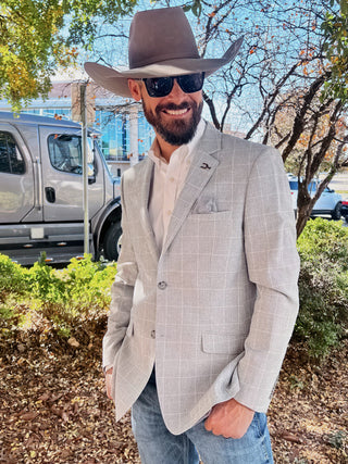 Man wearing a gray suit and cowboy hat outdoors with trees and vehicles in the background at WRCA Rodeo in Amarillo, TX. 