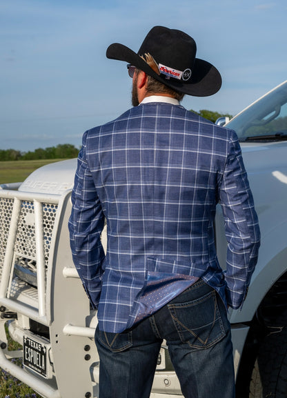 Man wearing a blue checkered jacket and black cowboy hat standing in front of a white truck.