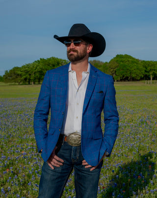 Man wearing a blue blazer and cowboy hat standing in a field with wildflowers.