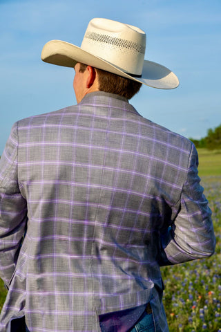 Man wearing a gray checkered jacket and white cowboy hat in an outdoor setting.