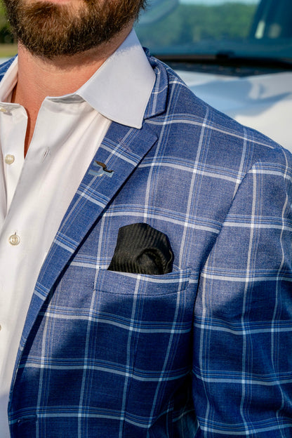 Man wearing a blue checkered sport coat over a white shirt with a black pocket square.