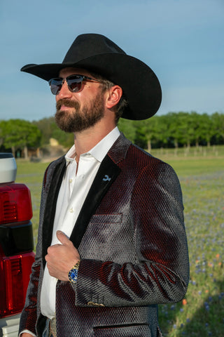 Man wearing a black cowboy hat and sunglasses in an outdoor setting with trees and a clear sky.
