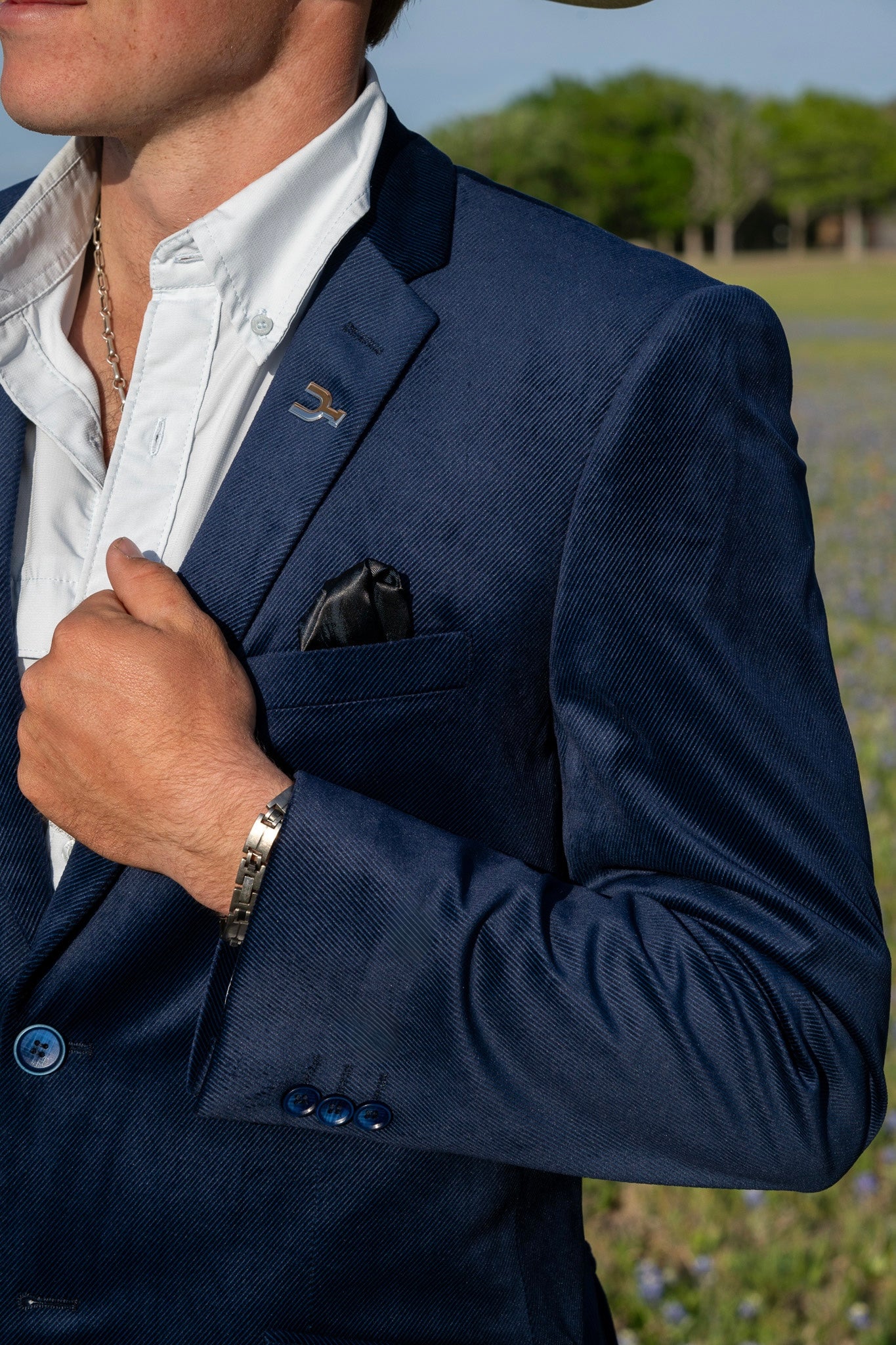 Man wearing a navy blazer with a white shirt and a field in the background. Texas bluebonnet pasture, branded Cowboy Sport Coat. Found in Texas. Made for cowboys to where in summer. Lightweight Western Blazer.