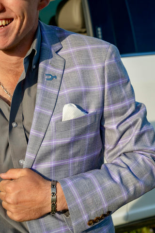 Man wearing a gray checkered suit jacket with a blue shirt and white pocket square.