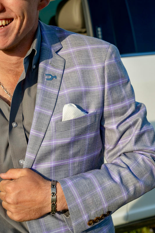 Man wearing a gray checkered suit jacket with a blue shirt and white pocket square.